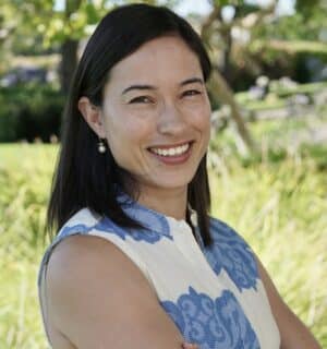 Headshot of Aiyana Mourtos smiling with greenery in background.