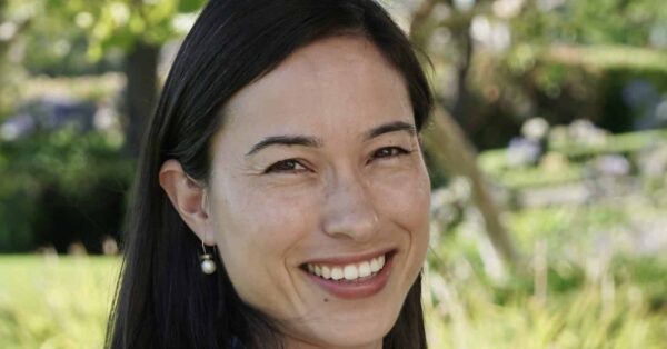 Headshot of Aiyana Mourtos smiling with greenery in background.