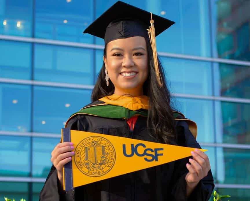 Carol holding UCSF flag in graduation attire