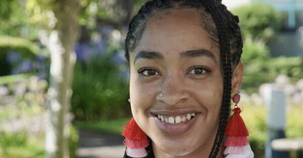 Mysia Pierce Lewis smiling for her headshot with greenery in the background and red earrings.