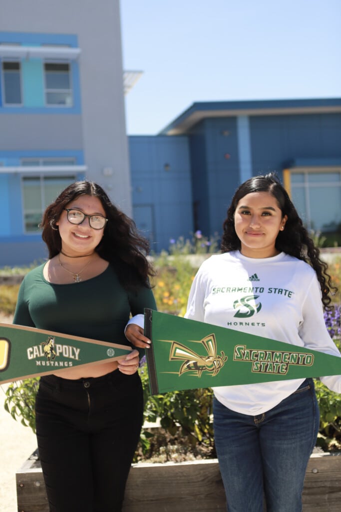Photo of two female students holding pennants of their college