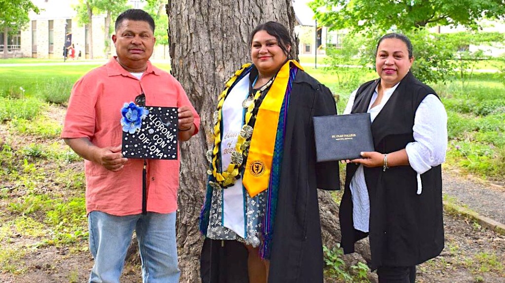 Carol wearing grad attire in the middle of her parents who are holding her grad cap and diploma