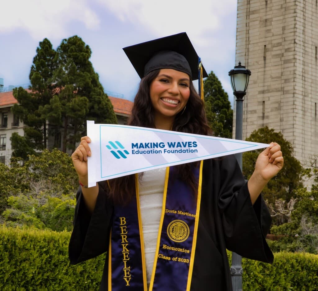 Doris Martinez in her cap and gown holding a MWEF banner at UC Berkeley
