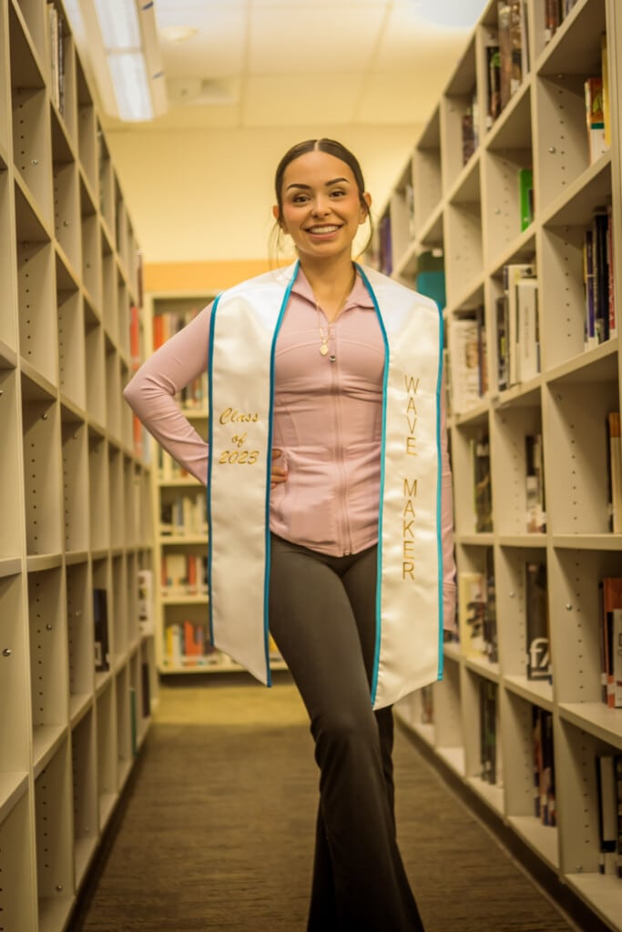 Dayannara Martinez stands in between two library stacks and psoes with a white Making Waves stole