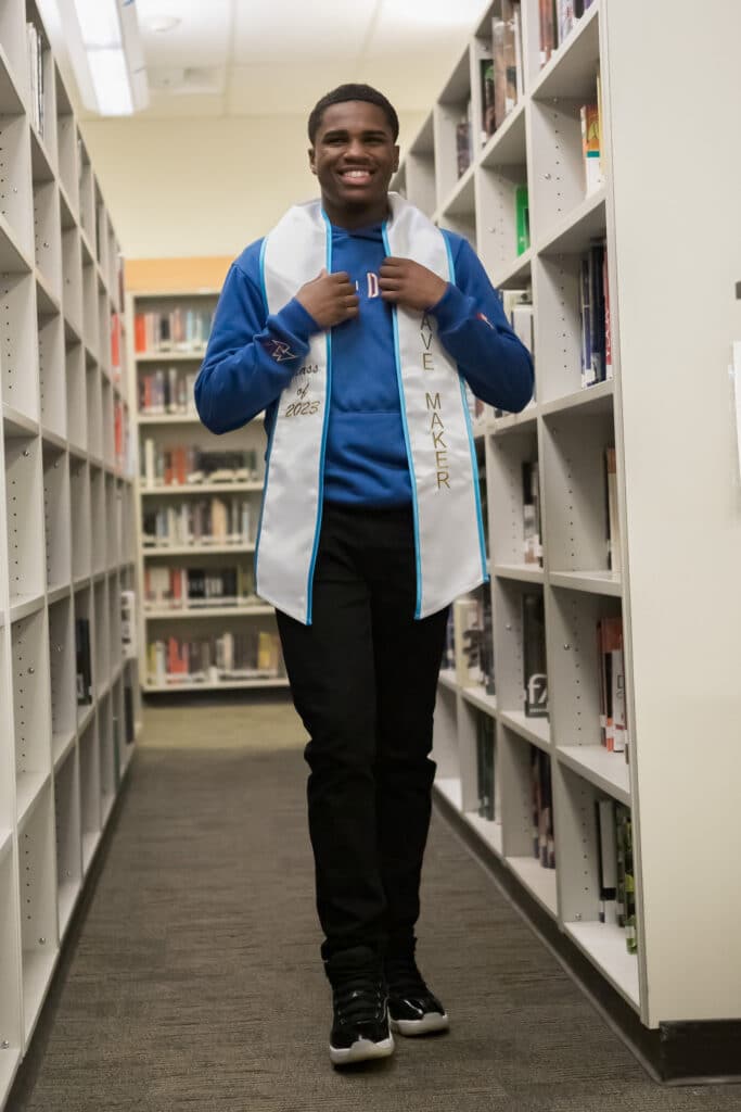 Erick Jones stands in between two library stacks and psoes with a white Making Waves stole