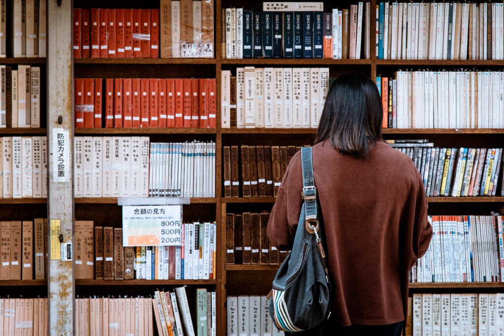 Photo of woman at a library looking at books wearing a brown cardigan