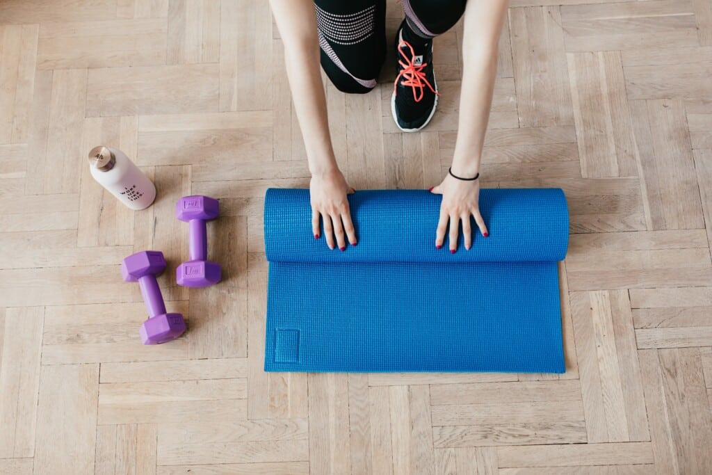 Photo of a woman rolling up a yoga mat and two dumbbells next to her