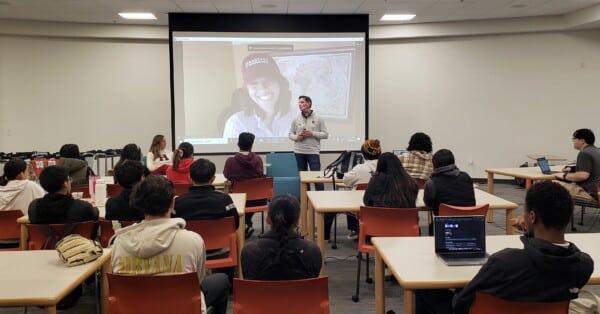 Person speaking in front of group of students with screen pulled down in background
