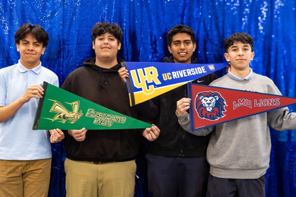 Students holding college pennants for Sac State, UC Riverside, and LMU