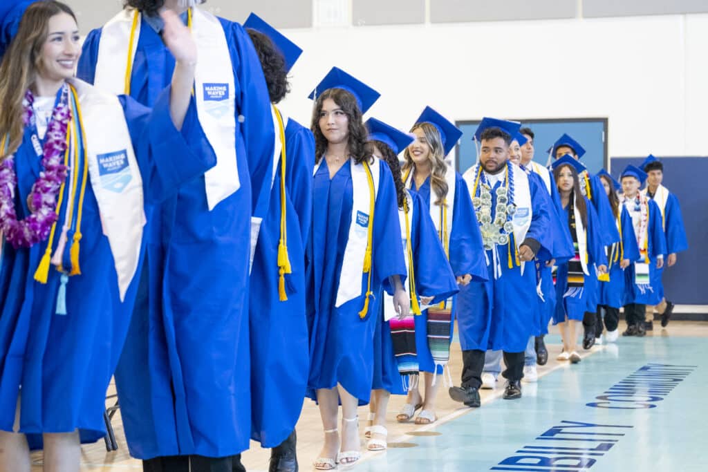 Students in blue caps and gowns walking into graduation