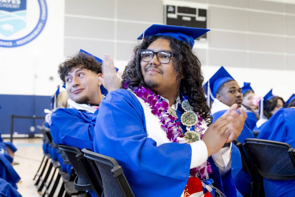 Students in blue caps and gowns clapping