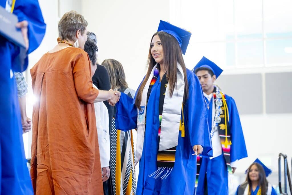 Student in blue cap and gown shaking person's hand on stage