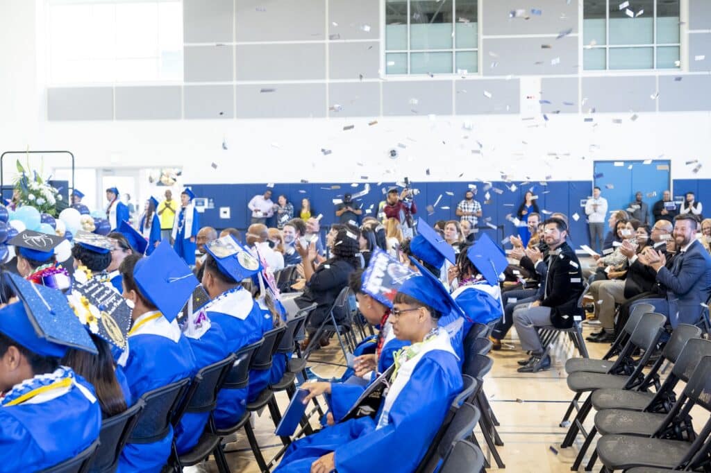Crowd of grads in blue caps and gowns with confetti falling