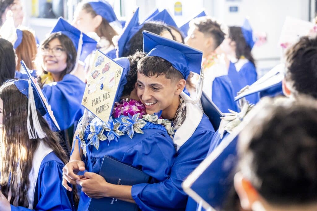 Two students in caps and gowns hugging