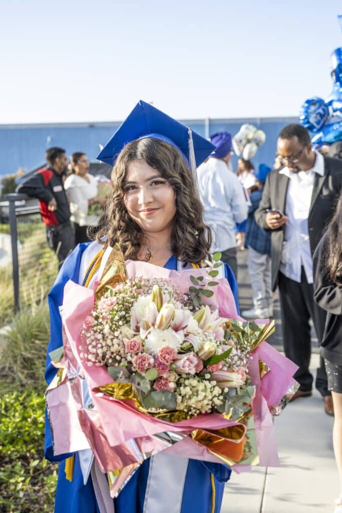 Student wearing grad cap and holding large bouquet of flowers
